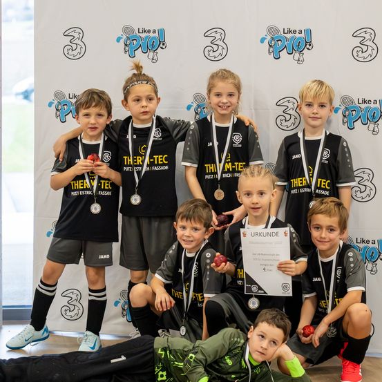 Eine Gruppe junger Athleten posiert für ein Foto mit Medaillen und Urkunden vor einer Wand mit Sportlogos.