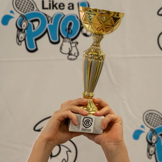 Eine Person hält einen goldenen Pokal mit einer weißen Basis vor einer Wand mit einem Sportclub-Logo.
