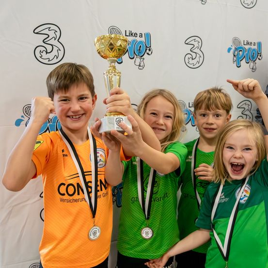 Fünf Kinder in Sporttrikots posieren mit einem goldenen Pokal und zeigen ihre Medaillen, um ihren Sieg zu feiern.