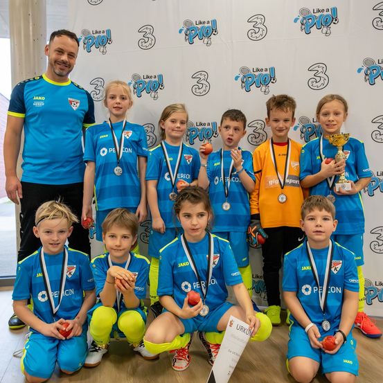 Eine Gruppe junger Athleten mit Medaillen und Äpfeln, die vor einem weißen Hintergrund mit Sportlogos stehen und für ein Foto posieren.