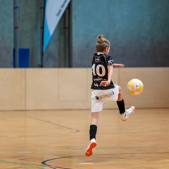 Ein junger Junge in einem Trikot tritt einen Fußball in einer Sporthalle. Der Junge trägt ein schwarzes Trikot mit der Nummer 10.