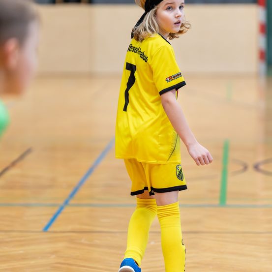 Ein junges Mädchen in einem gelben Fußballtrikot mit der Nummer 7 läuft auf einem Spielfeld. Sie schaut konzentriert nach vorne.