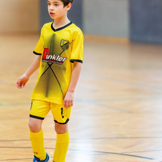 Ein junger Junge in einem gelben Fußballtrikot läuft auf einem Hallenplatz. Das Trikot hat das Wort Dunkler darauf.