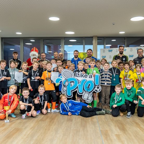 Eine Gruppe junger Athleten und Trainer posiert für ein Foto mit Medaillen und Auszeichnungen in einer Halle. Der Weihnachtsmann ist ebenfalls anwesend und fügt der festlichen Atmosphäre etwas hinzu.