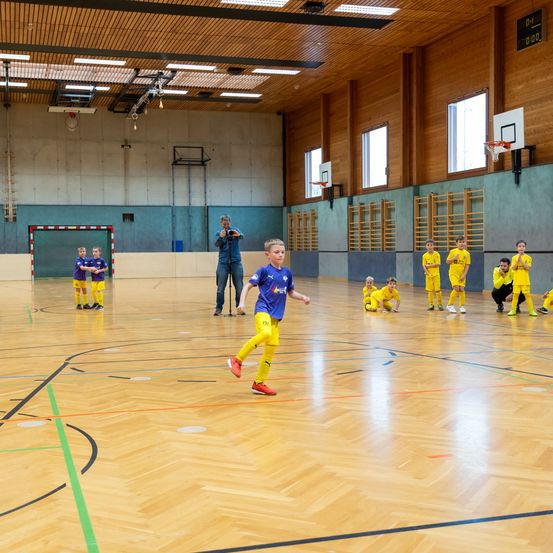 Indoor-Fußballtraining mit jungen Jungen. Ein Junge läuft auf den Ball zu. Die anderen warten in ihren Positionen.