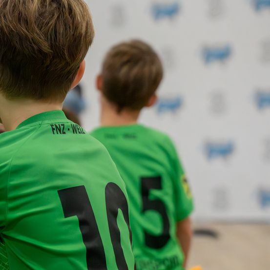 Zwei Jungen in grünen Fußballtrikots stehen vor einer unscharfen Wand. Der Junge vorne hat die Nummer 10 auf seinem Trikot.