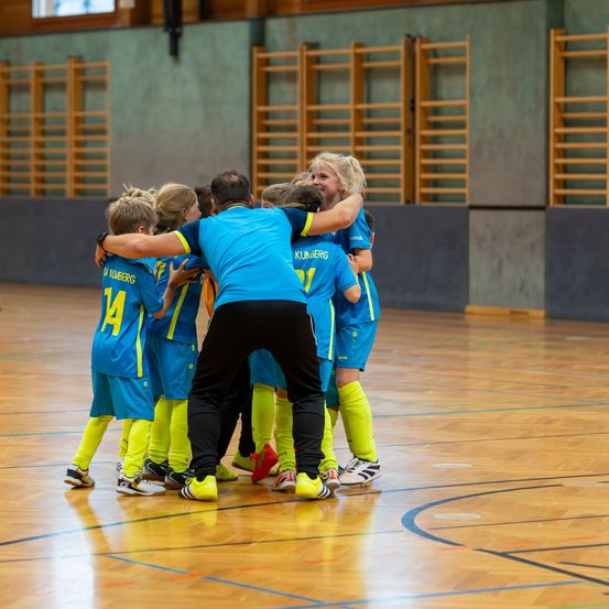 Ein Fußballtrainer schließt sich mit einer Mannschaft junger Spieler auf einem Spielfeld ab und feiert einen Sieg.