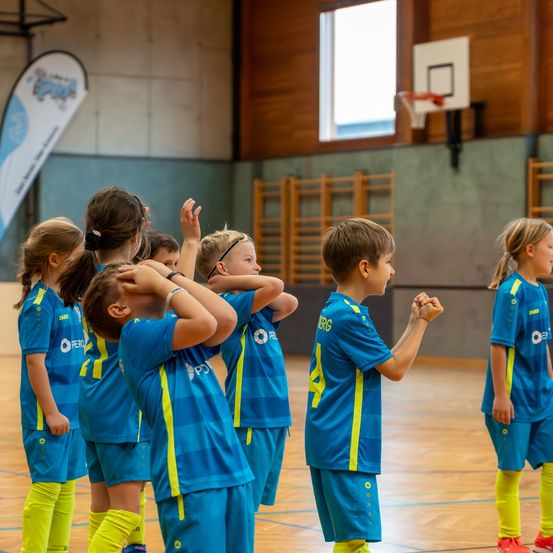 Eine Gruppe junger Kinder in blauen und gelben Uniformen steht auf einem Basketballplatz und wartet scheinbar auf Anweisungen.