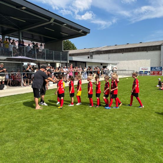 Eine Gruppe junger Fußballspieler in roten Trikots, auf dem Feld aufgestellt, mit Zuschauern, die von den Tribünen aus zuschauen.