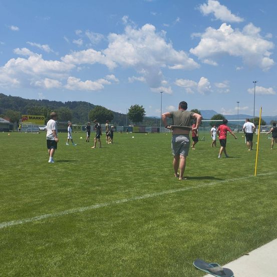 Mehrere Menschen in Freizeitkleidung sind auf einem Fußballfeld. Sie scheinen ein Spiel zu üben.