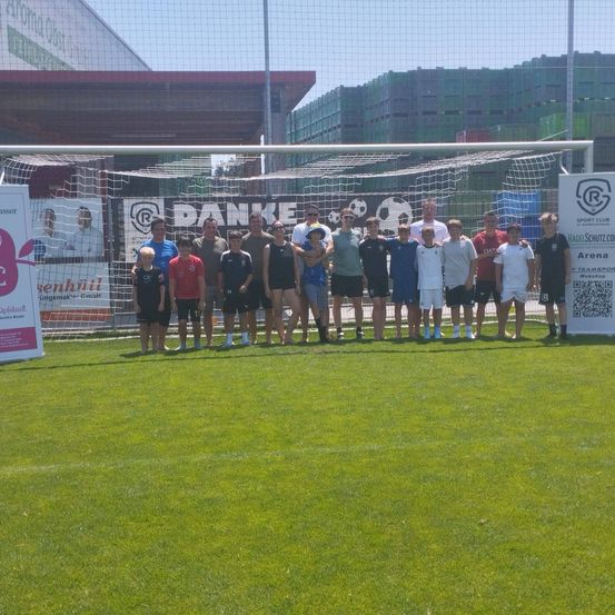 Eine Gruppe junger Fußballspieler steht vor einem Tor und posiert für ein Foto. Sie tragen verschiedenfarbige Trikots.