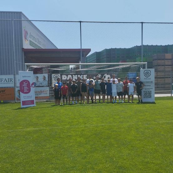 Eine Gruppe von Menschen, wahrscheinlich eine Fußballmannschaft, posiert für ein Foto auf einem Fußballfeld mit einem Tor im Hintergrund.