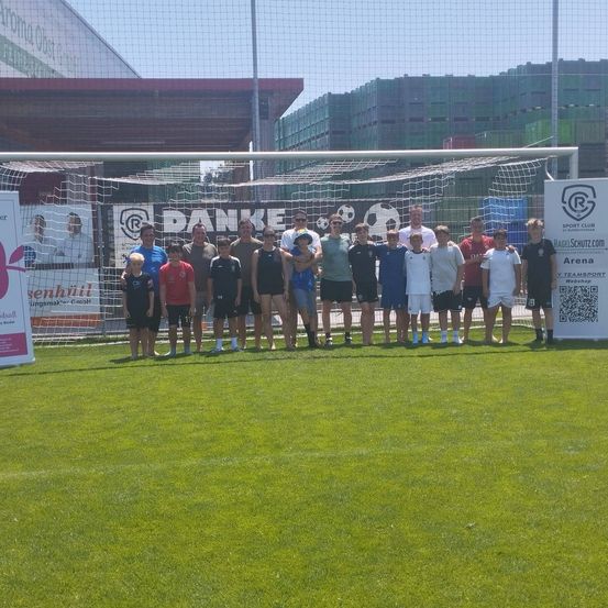 Eine Gruppe von Menschen posiert für ein Foto auf einem Fußballfeld vor einem Tor mit Sponsorenbannern dahinter.