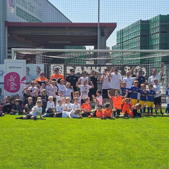 Eine Gruppe junger Spieler und Trainer posiert für ein Foto auf einem Fußballfeld vor einem Tornetz.