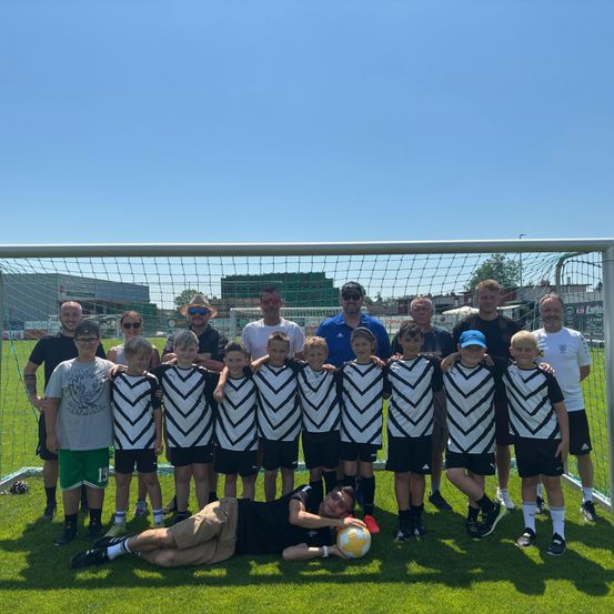 Eine Fußballmannschaft posiert für ein Gruppenfoto vor einem Tor, die Spieler tragen schwarze und weiße Trikots.