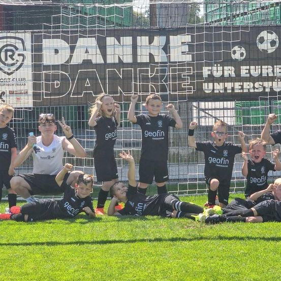 Eine Gruppe junger Fußballspieler, Jungen und Mädchen, posiert für ein Foto vor einem Tornetz, mit einem Banner mit der Aufschrift Danke.
