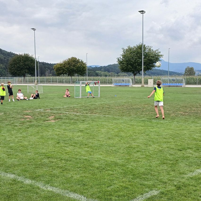 A group of children in green uniforms are playing soccer on a field with a soccer ball in the air.