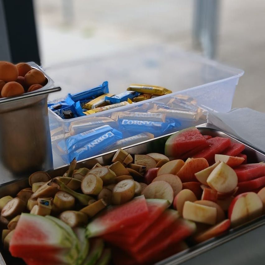 A tray with sliced watermelon, bananas, and apples, along with a container of cookies and a bowl of eggs.