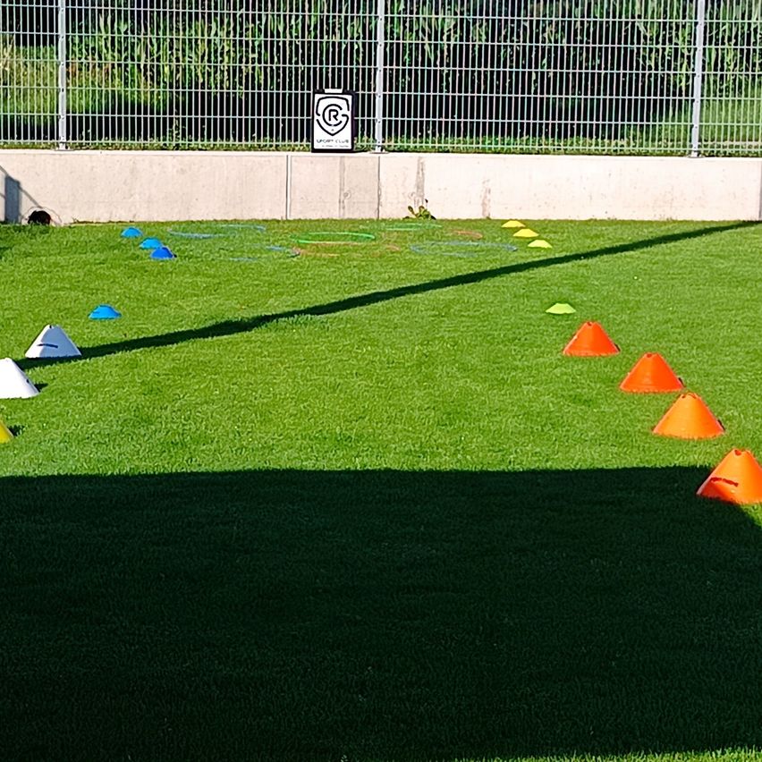 A sports field with artificial turf, featuring a metal fence, a sign, and various colored cones and markers scattered across the field.