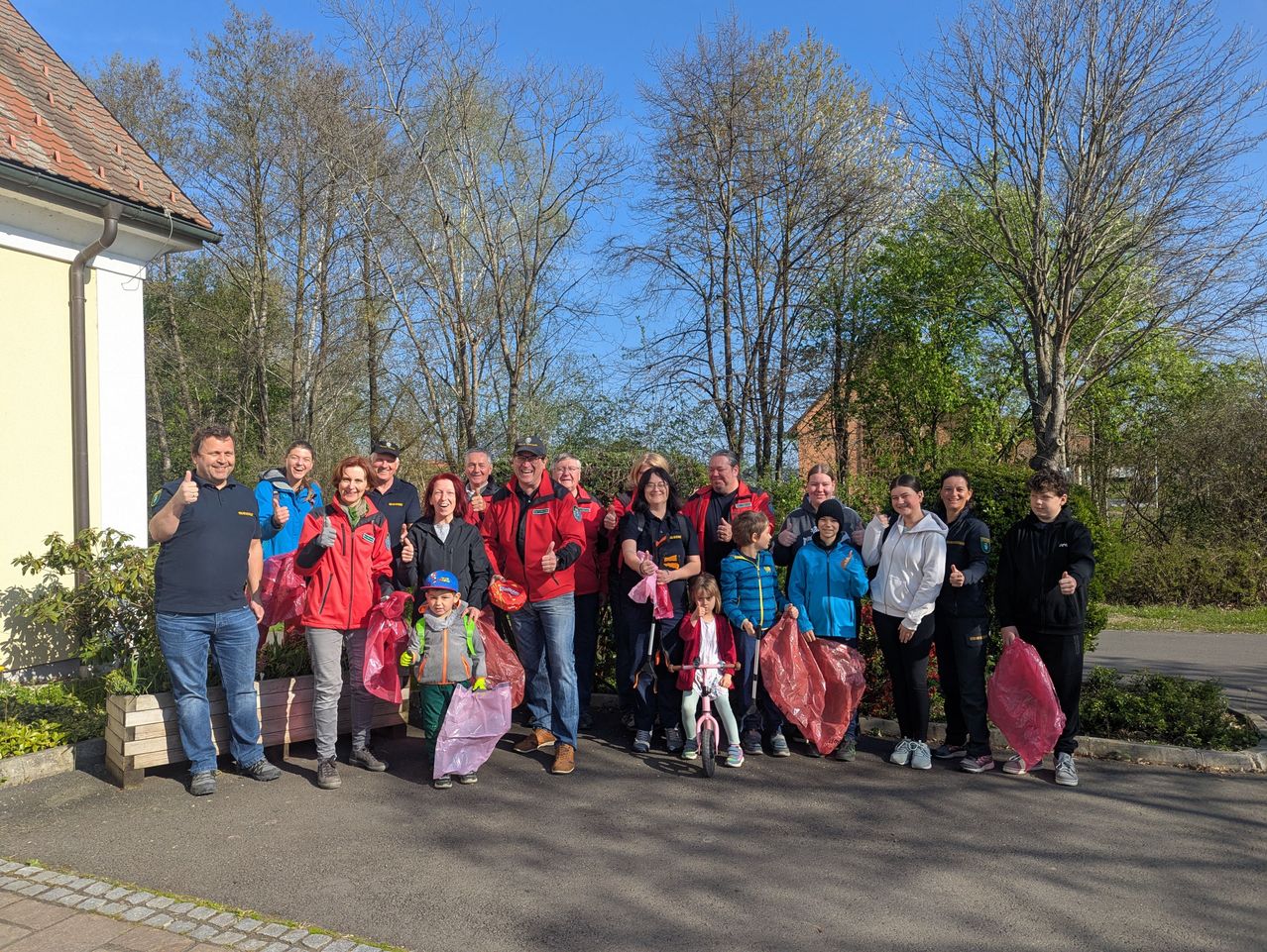 Eine große Gruppe von Menschen in roten Jacken und mit Plastiktüten steht auf einer Straße.