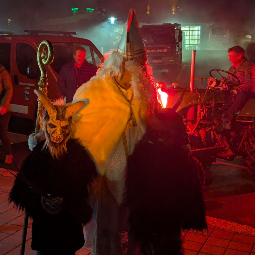 Eine Person in einem Kostüm mit einem Stab steht in der Nähe eines Fahrzeugs mit zwei Personen im Hintergrund.