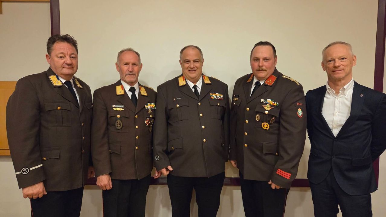 Vier Männer in Militäruniformen stehen zusammen vor einer weißen Wand. Sie lächeln und scheinen für ein Foto zu posieren.