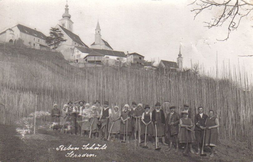 Schwarz-Weiß-Foto einer Gruppe von Menschen, die in einem Feld stehen, mit einer Kirche im Hintergrund.