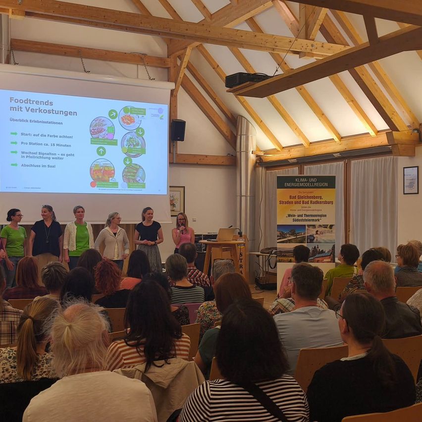 Eine Gruppe von Menschen in grünen Shirts steht vor einer Leinwand mit Essenstrends, umgeben von einem Publikum in einem hölzernen Raum.