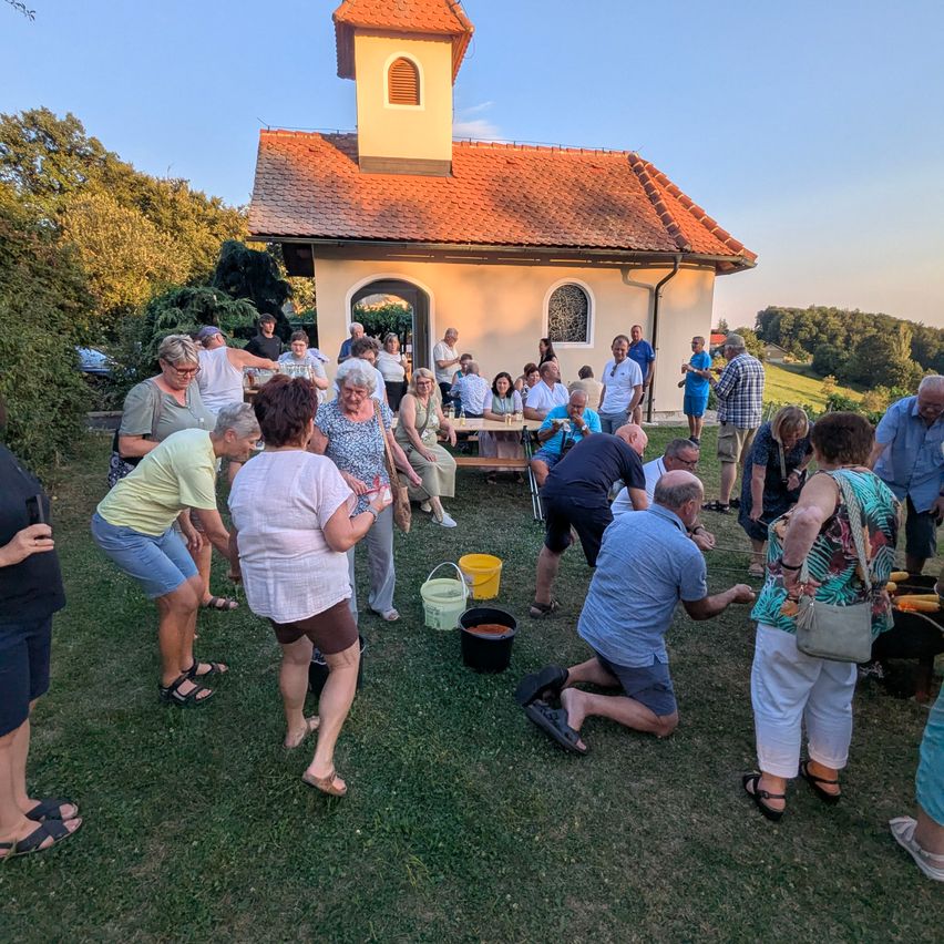 Eine Gruppe von Menschen versammelt sich vor einer kleinen Kapelle, einige knien und andere stehen, mit einem Tisch und Eimern in der Nähe.