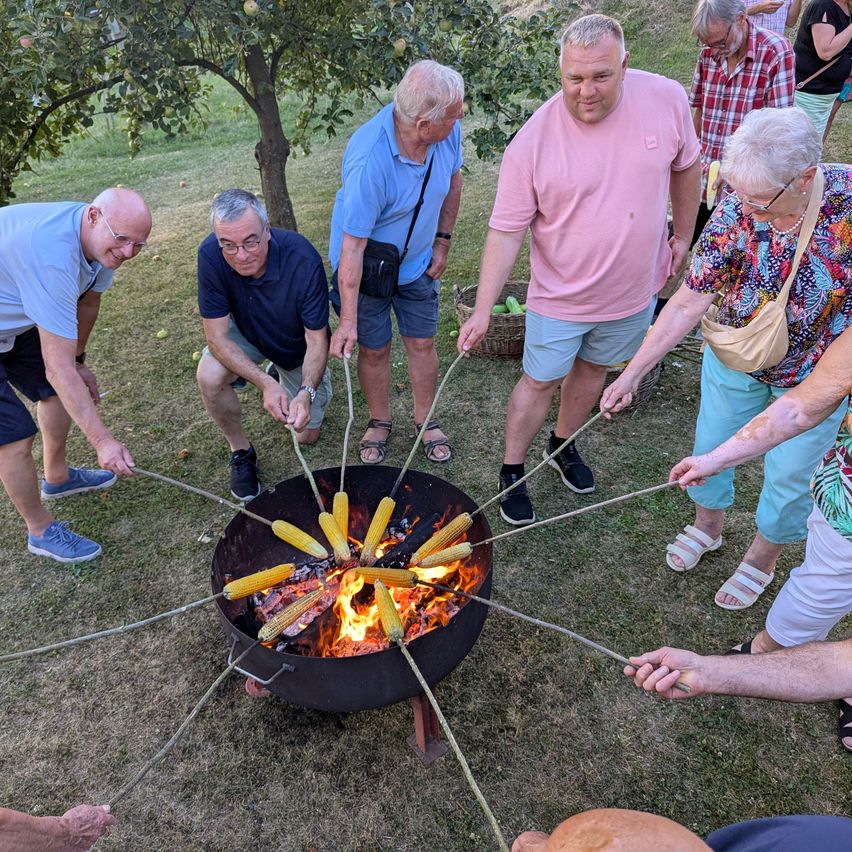 Eine Gruppe von Menschen röstet Maiskolben über einem Feuer im Freien.