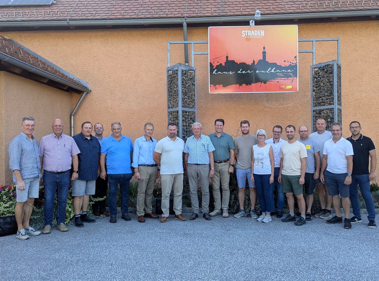 A group of men and women pose for a photo in front of a building with a sign that reads 'Straden'.