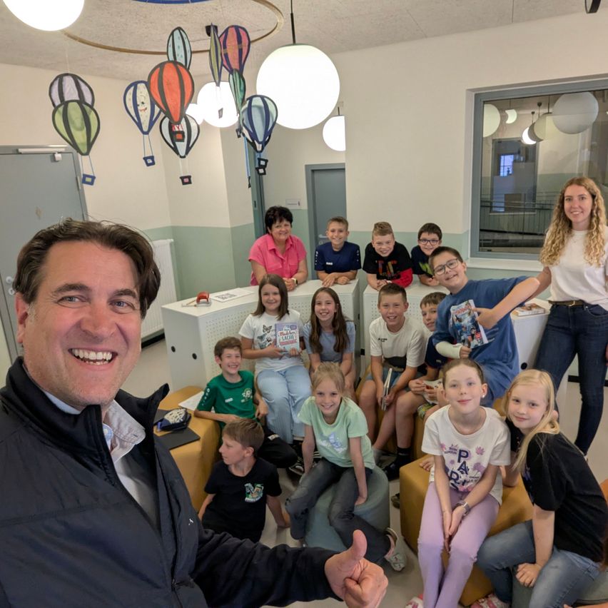 Eine Gruppe von Kindern und Erwachsenen in einem Raum, lächelnd und posierend für ein Foto. Heißluftballons hängen von der Decke.