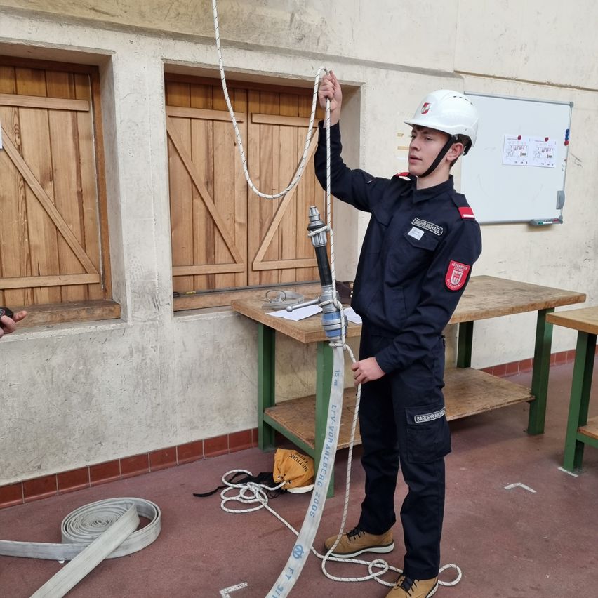 Eine Person in Uniform hält ein Seil und scheint in einem Raum mit Holzfenstern und Tischen zu trainieren.