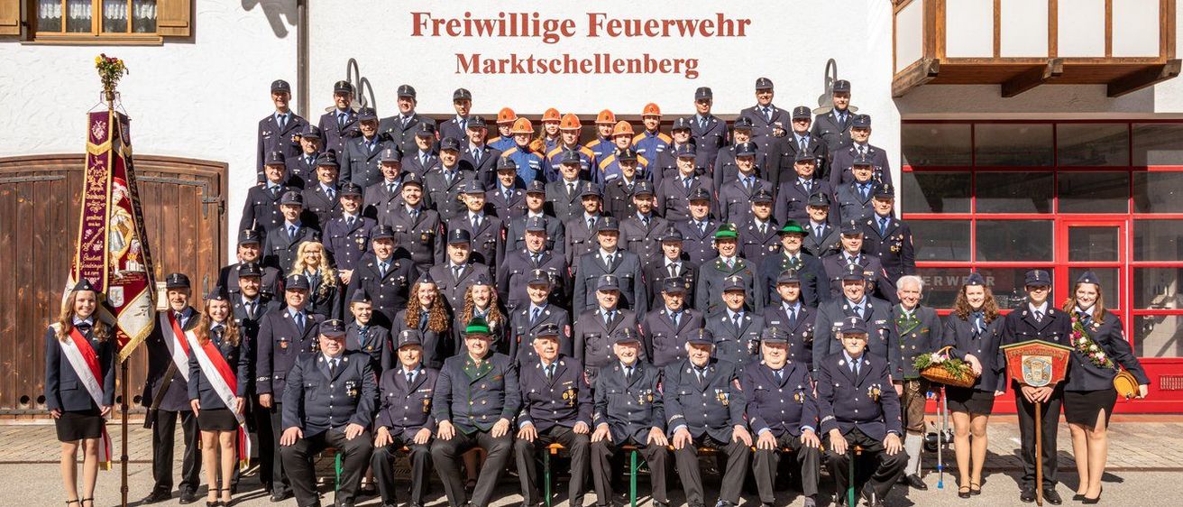 Eine große Gruppe von Feuerwehrleuten in Uniform, die vor einem Gebäude stehen, auf dem 'Freiwillige Feuerwehr Marktschellenberg' steht.