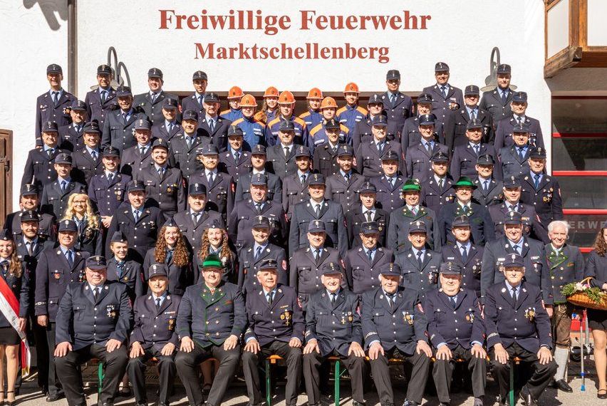 Eine große Gruppe von Feuerwehrleuten in Uniform, die vor einem Gebäude stehen, auf dem 'Freiwillige Feuerwehr Marktschellenberg' steht.