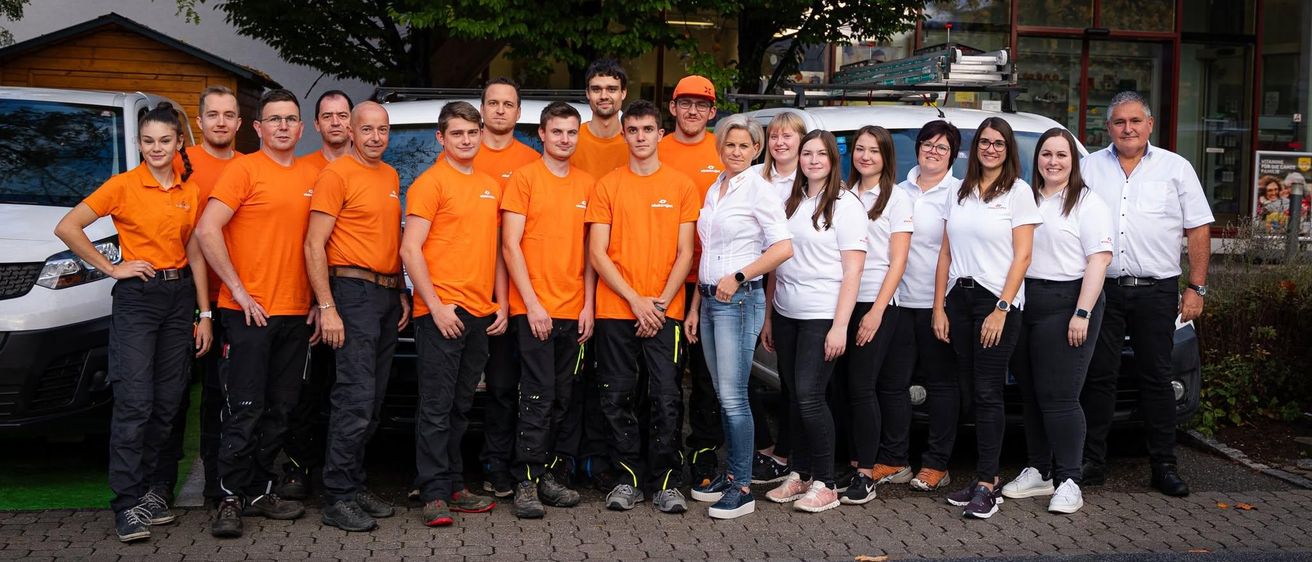 Eine Gruppe von Menschen in orangefarbenen und weißen Uniformen posiert für ein Foto vor einem Fahrzeug.