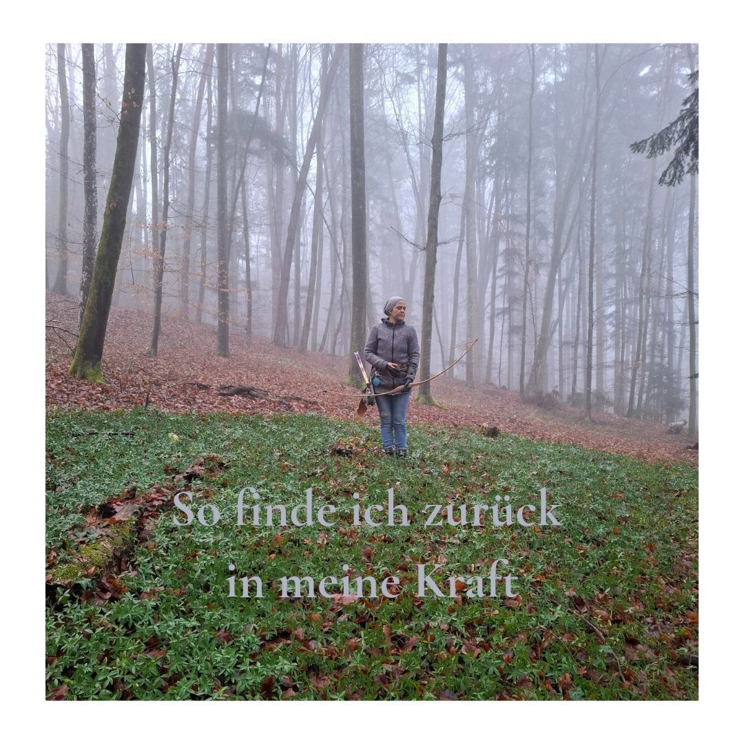 Eine Person steht in einem nebligen Wald, einen Stock in der Hand, angezogen in einer grauen Jacke und Jeans. Der Wald ist dicht mit Bäumen und Grün bedeckt. Der Boden ist mit Gras und Laub bedeckt. Die Person scheint nach etwas zu suchen.