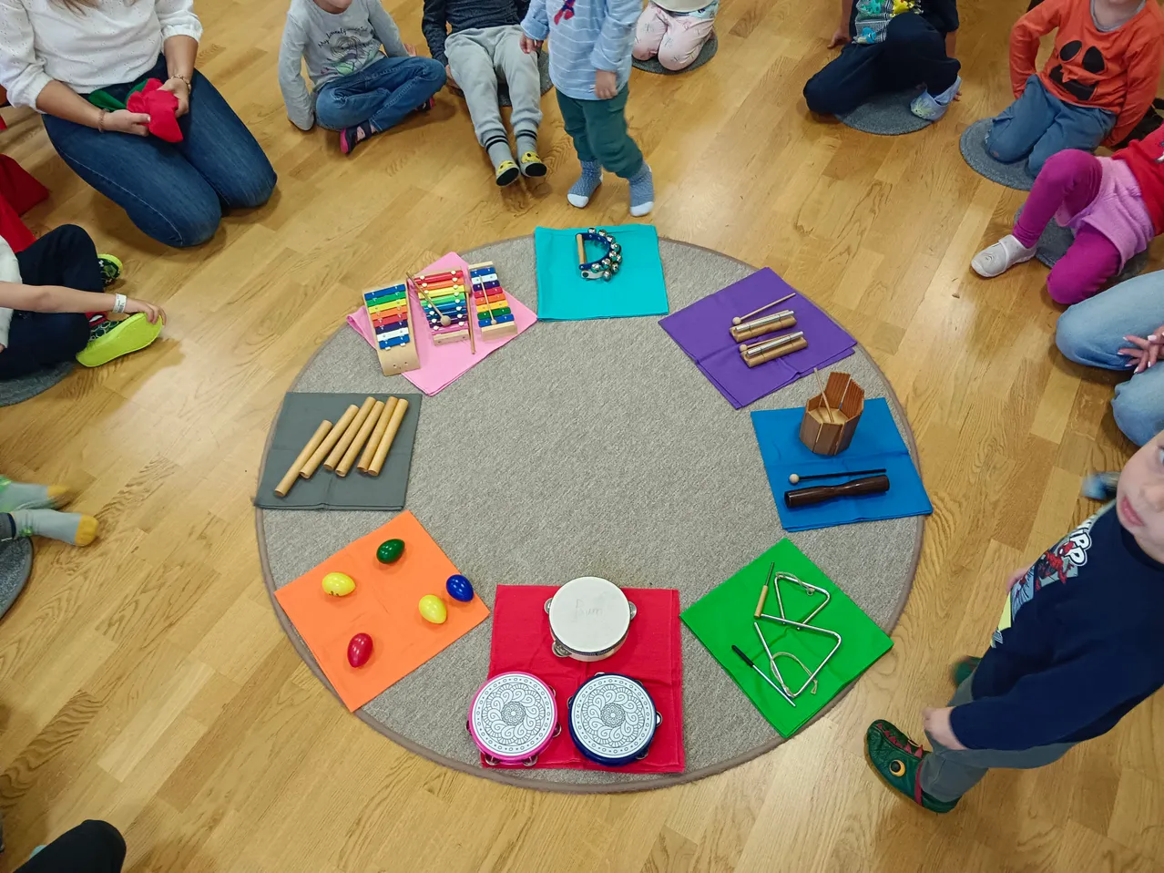 Eine Gruppe von Kindern sitzt in einem Kreis um einen runden Tisch mit verschiedenen Musikinstrumenten darauf.