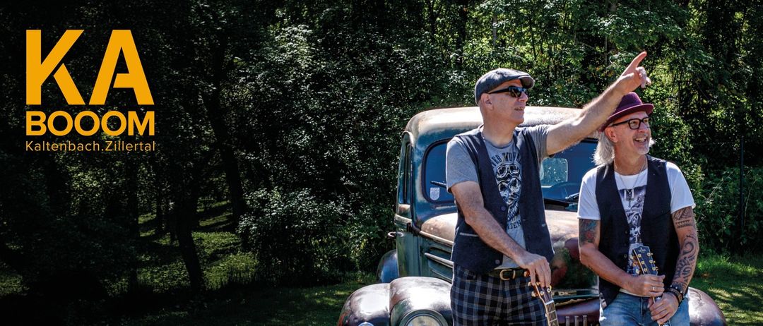 Zwei Männer in Hüten und Sonnenbrillen stehen neben einem Oldtimer und halten Gitarren, mit einem Schild, das 'Die Oldies' und einen Zeitplan anzeigt.