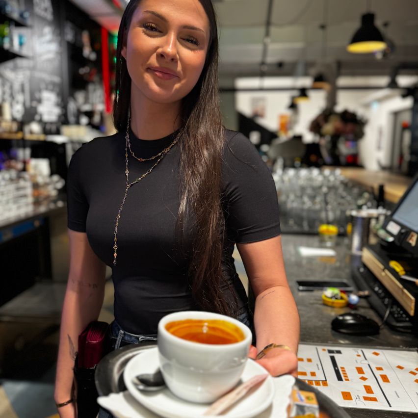 Eine Barista hält eine Kaffeetasse mit Löffel auf einer Untertasse in einem Café.