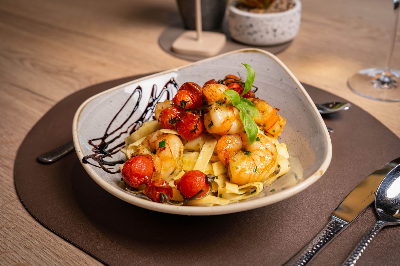 Ein Gericht mit Pasta, Garnelen, Kirschtomaten und Basilikumblättern auf einem Holztisch.