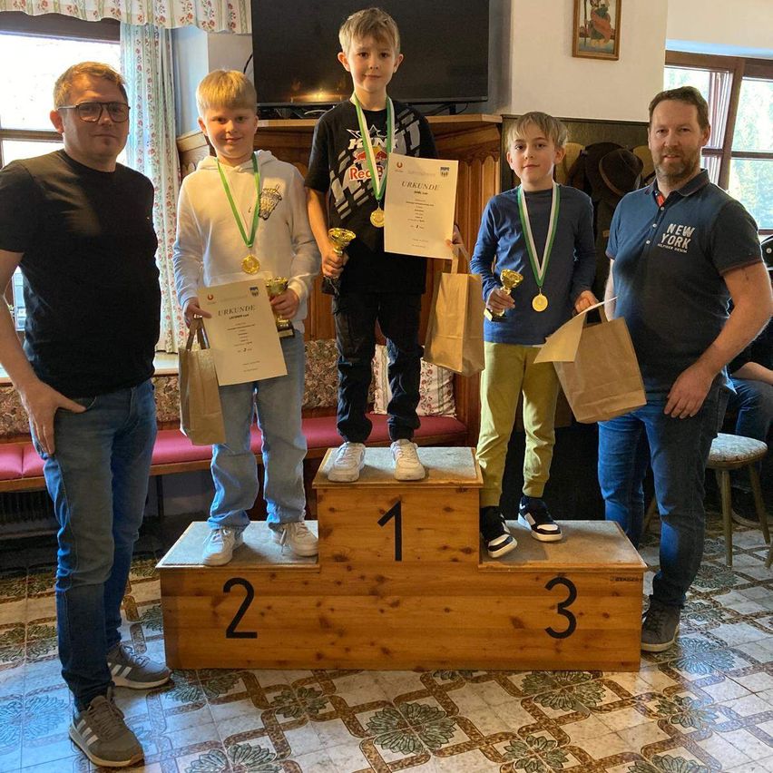 Fünf Jungen stehen auf einem hölzernen Podest, halten Medaillen und Urkunden in den Händen. Der Junge in der Mitte trägt ein schwarzes T-Shirt mit einem Red-Bull-Logo und die anderen verschiedene Farben. Das Podest hat die Zahlen 1, 2 und 3.