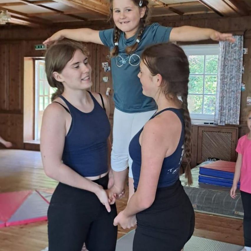 Drei Frauen in einem Raum mit einem Mädchen auf ihren Schultern. Zwei der Frauen lächeln und schauen sich an. Das Mädchen auf ihren Schultern hält ihre Hände.