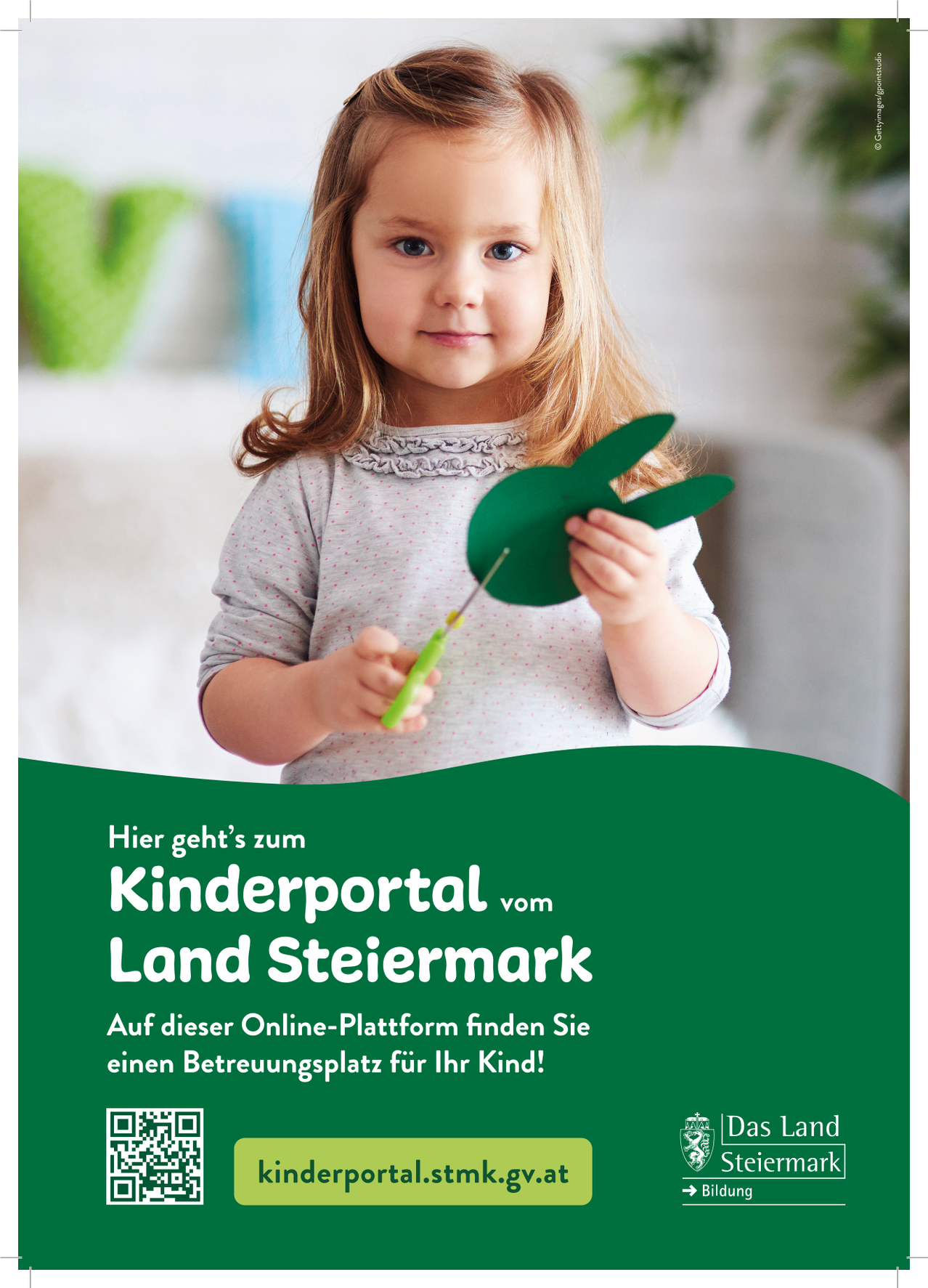 A young girl is holding a green paper craft shaped like a rabbit. She is smiling and looking at the camera. The image is from the Kinderportal of Land Steiermark.