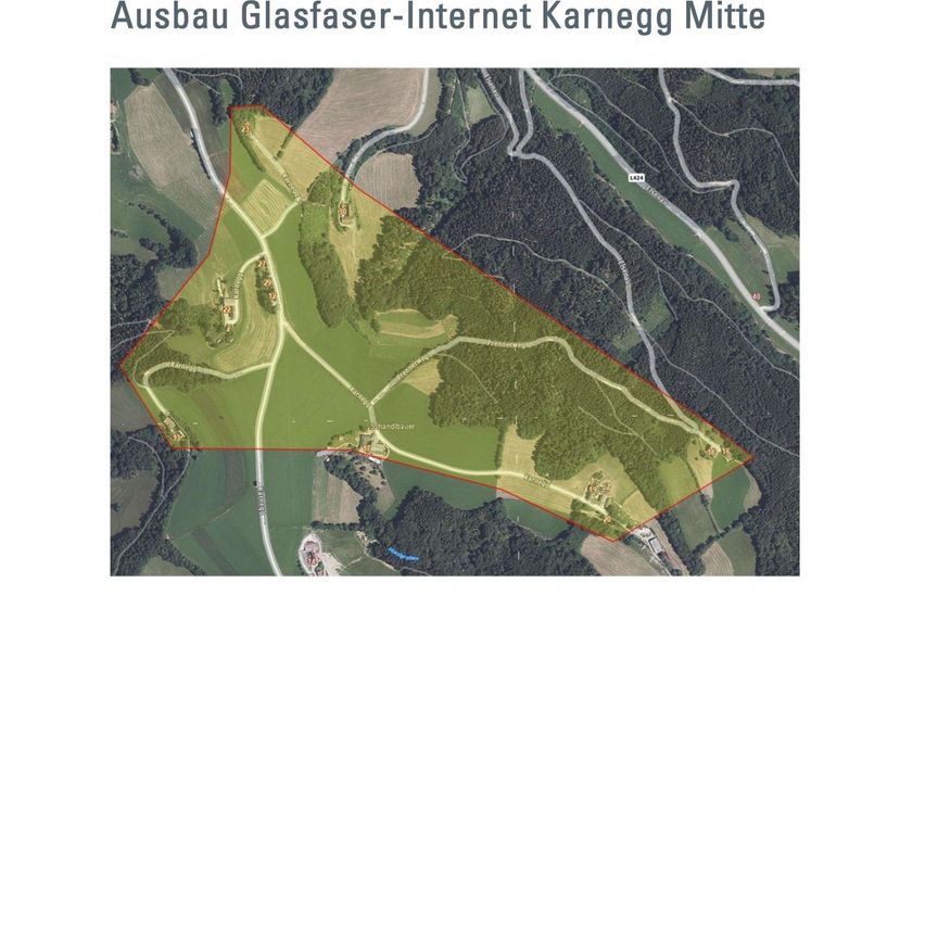 Aerial view of a rural area with green fields, a winding road, and a red outline highlighting a specific area.