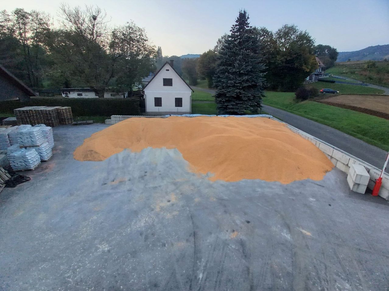 Eine Luftaufnahme eines Grundstücks mit einem großen Getreidehaufen auf dem Boden vor einem weißen Haus und Bäumen.