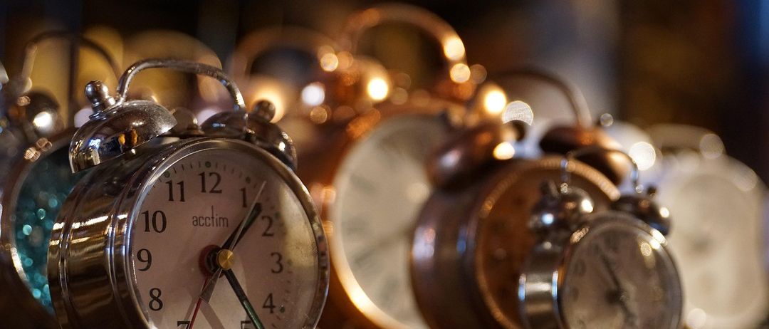 Eine Sammlung von Vintage-Weckern mit metallischen Oberflächen, einer zeigt die Zeit 11:09, angeordnet auf einer Holzoberfläche.