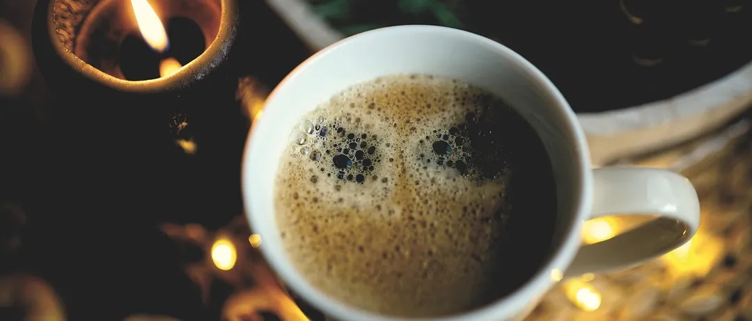 Eine Nahaufnahme einer Tasse Kaffee mit einer Kerze und Essen im Hintergrund.