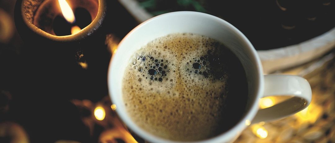 Eine Nahaufnahme einer Tasse Kaffee mit einer Kerze und Essen im Hintergrund.