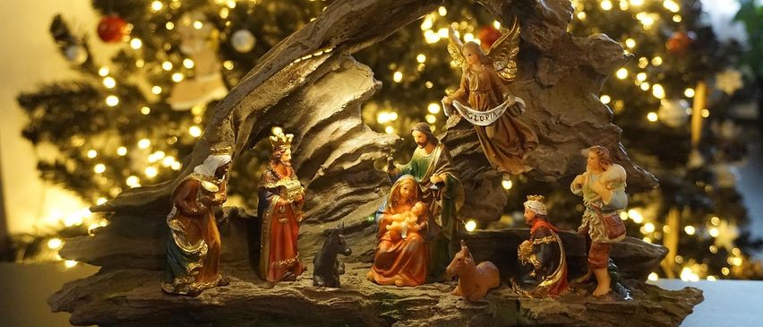 Vor einem Weihnachtsbaum ist eine Krippe aufgestellt. Die Szene zeigt Maria, Josef, das Baby Jesus, einen Engel und die drei Weisen. Der Hintergrund ist unscharf und hebt die Krippe hervor.
